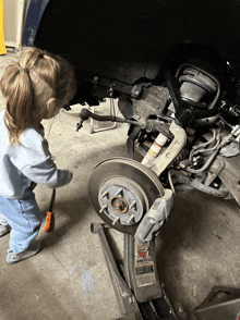 a little girl is working on a car with a jack that says eagle claw