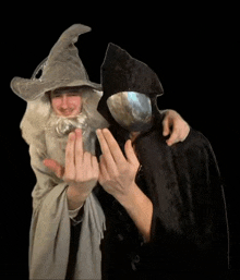 a man in a wizard costume and a man in a grim reaper costume are making a middle finger sign .