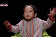 a little boy in a striped shirt is sitting in a green chair with his hands in the air .