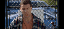 a man wearing a plaid shirt is making a funny face in front of a chain link fence