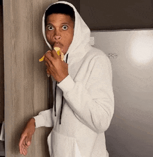a man wearing a hoodie is eating a banana
