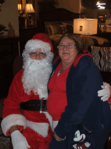 a woman wearing a mickey mouse sweatshirt sits next to a man dressed as santa claus