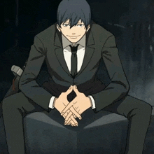 a man in a suit and tie is sitting with his legs crossed and his hands folded