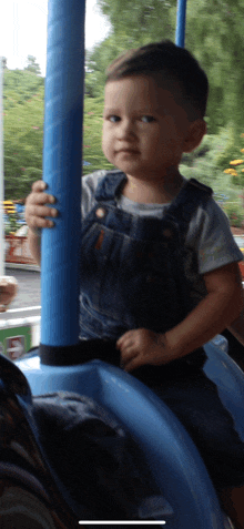 a little boy in overalls is sitting on a blue ride