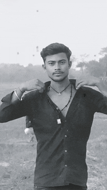 a man in a black shirt with a necklace around his neck stands in a field