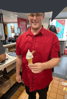 a man in a red shirt is holding a cone of ice cream