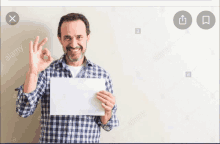 a man in a plaid shirt is holding a piece of paper and giving the ok sign .