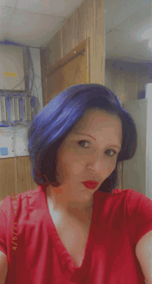 a woman with blue hair is wearing a red shirt and taking a picture of herself