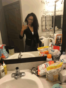 a woman taking a selfie in front of a bathroom mirror with a bag of value size wipes on the counter