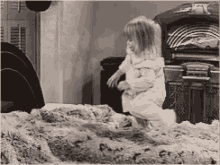 a little girl is kneeling on a bed in front of a jukebox in a black and white photo .