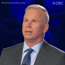 a man in a suit and tie stands in front of a microphone with the words family feud canada behind him