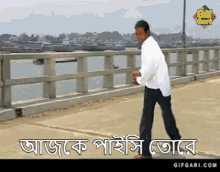 a man in a white shirt is walking across a bridge in front of a body of water with the words gifgari.com below him