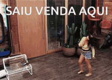 a woman is dancing in a living room with the words " saiu venda aqui " written on the wall behind her .