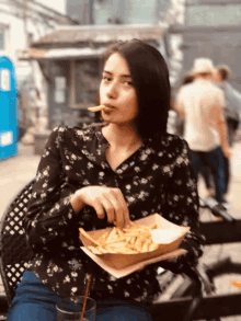 a woman in a floral shirt is eating french fries from a tray