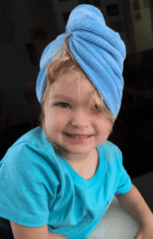 a little girl wearing a blue shirt has a blue towel wrapped around her head