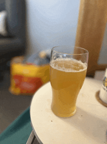 a glass of beer sits on a table in front of a bag of chips