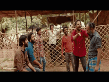 a group of men are standing in front of a wooden fence and one man is pointing at the camera