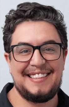 a man with glasses and a beard is smiling and wearing a black shirt .