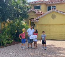 a family standing in front of a yellow house holding a sign that says " addres "