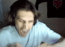 a man with long hair is wearing headphones and making a funny face while sitting in front of a computer .