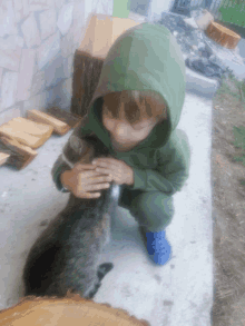 a young boy in a green hoodie petting a small cat