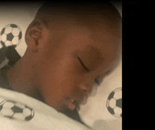 a young boy is sleeping on a bed with soccer balls on the sheets