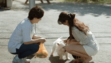 a man and a woman are kneeling down next to a small white dog on a leash .