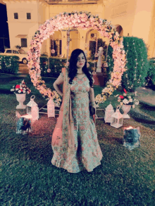 a woman stands in front of a floral arch