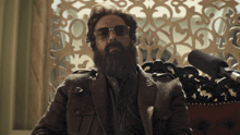 a man with a beard and sunglasses sits in front of a window