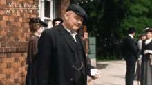 a man in a suit and hat is standing in front of a brick building with murdoch mysteries written on it