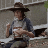 a young boy wearing a cowboy hat is eating from a bucket of food