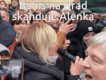 a woman screams into a microphone in front of a crowd with the words babis na hrad skanduje alenka above her