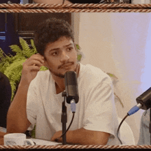 a man in a white shirt is sitting in front of a microphone with a cup of coffee on the table