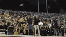 a man stands in front of a crowd at a football game wearing a black shirt with the word west on it