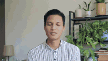 a man in a striped shirt with his eyes closed stands in front of a shelf full of potted plants