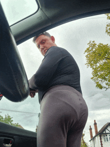 a man in a black shirt and grey pants is standing in a car