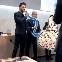 a man in a suit is holding a thumbs up sign in front of a brain .