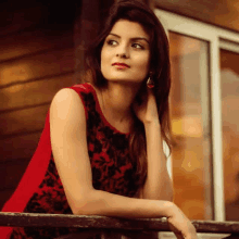 a woman in a red dress is leaning on a railing and looking out the window .