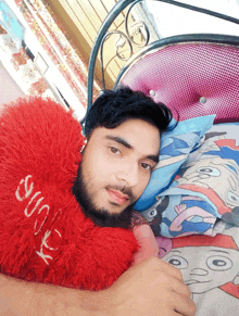 a man laying on a bed with a red heart shaped pillow that says jesus on it