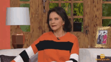 a woman in an orange and black striped sweater is sitting on a couch in front of a picture frame that says ventaneando