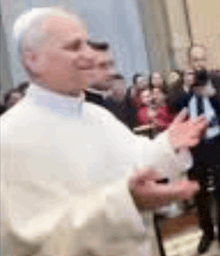 a man in a white robe is standing in front of a crowd with his hands outstretched .