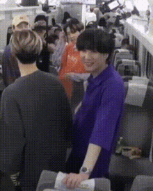 a man in a purple shirt is standing in front of a crowd of people on an airplane