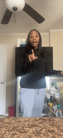 a woman standing in front of a refrigerator with a ceiling fan above her