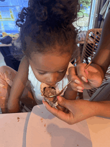 a little girl with curly hair is eating ice cream with a fork