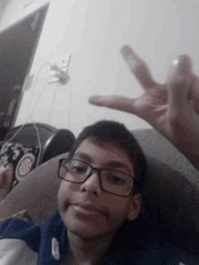 a young boy wearing glasses is giving a peace sign while sitting on a couch