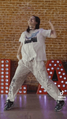 a woman in a white shirt and white pants is dancing in front of a red letter a