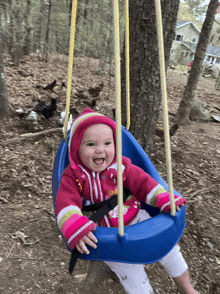 a baby in a pink sweater is swinging on a blue swing in the woods