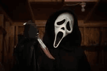 a person wearing a scream mask is holding a knife in a dark room .