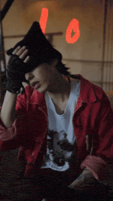 a man wearing a red jacket and a black hat is covering his face with his hands