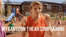 a woman stands in front of a playground with the words " my ears don 't hear complaining " above her